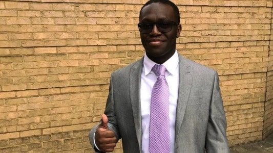 Deji Olatunji Wearing Grey suit and posing his thumb nail